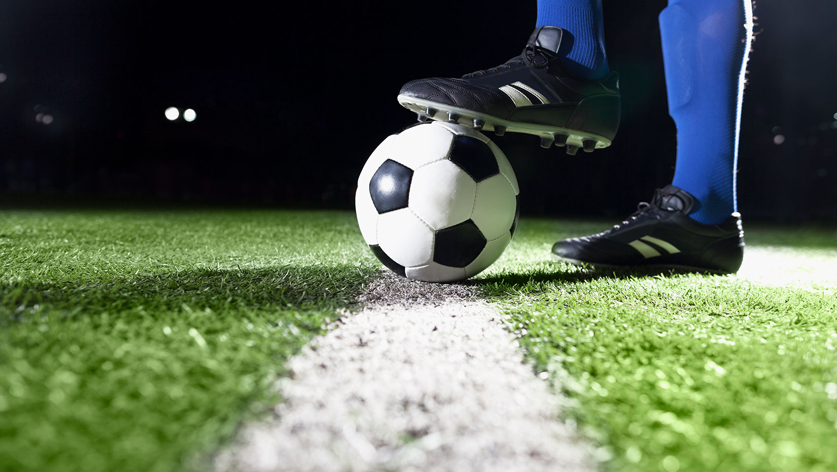 Soccer ball on pitch with player in blue socks