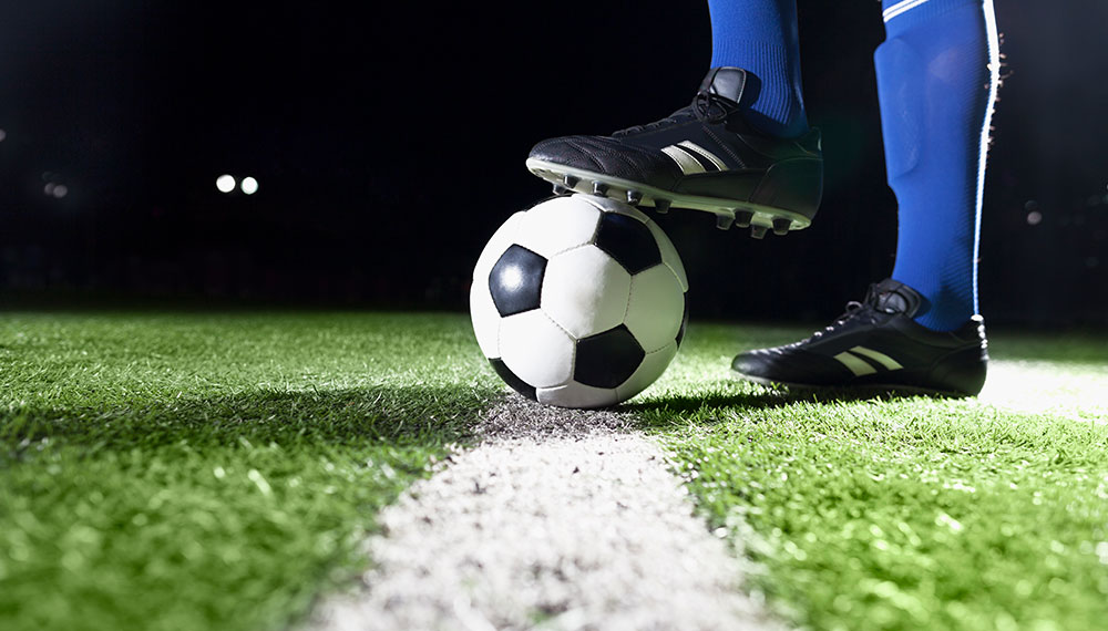 Soccer ball on pitch with player in blue socks